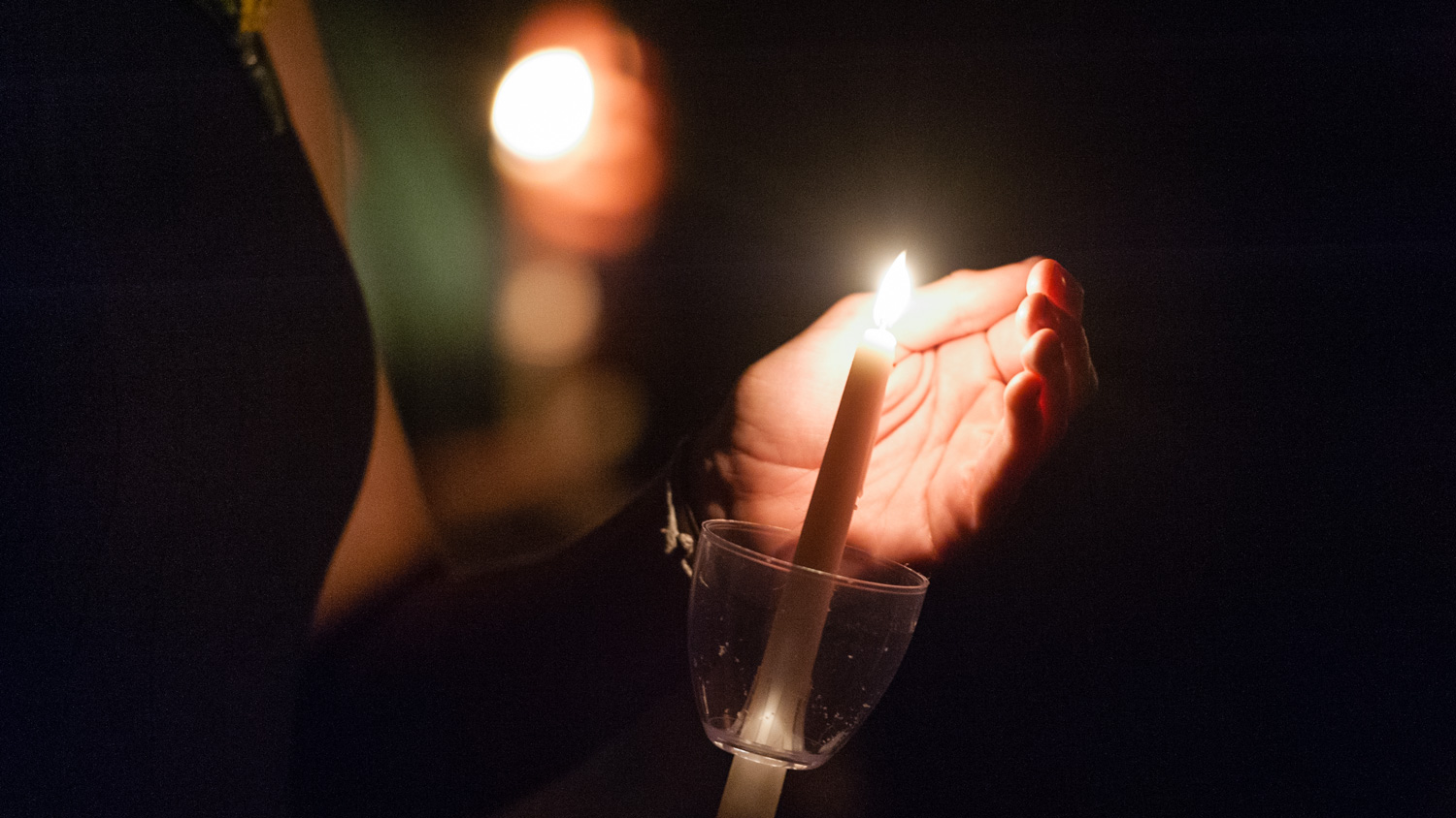 a hand shields the flame of a candle