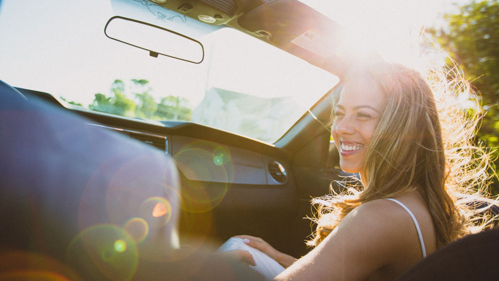 a woman smiling in the car with the sun shining behind her