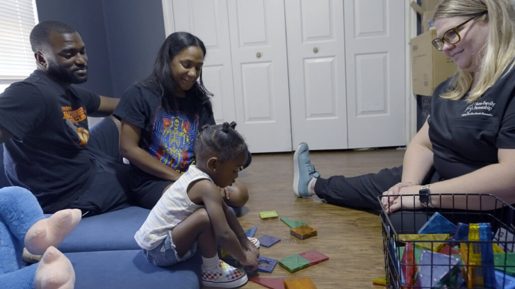 A child plays with toys as her parents and a nurse watch.