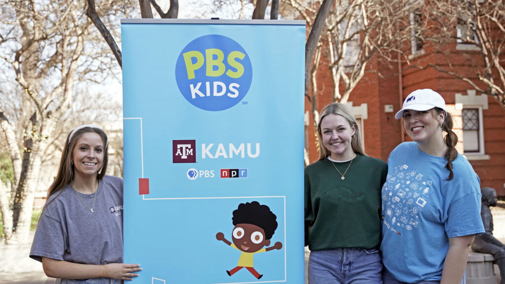 Elizabeth, Emily and Alex standing next to PBS KIDS banner