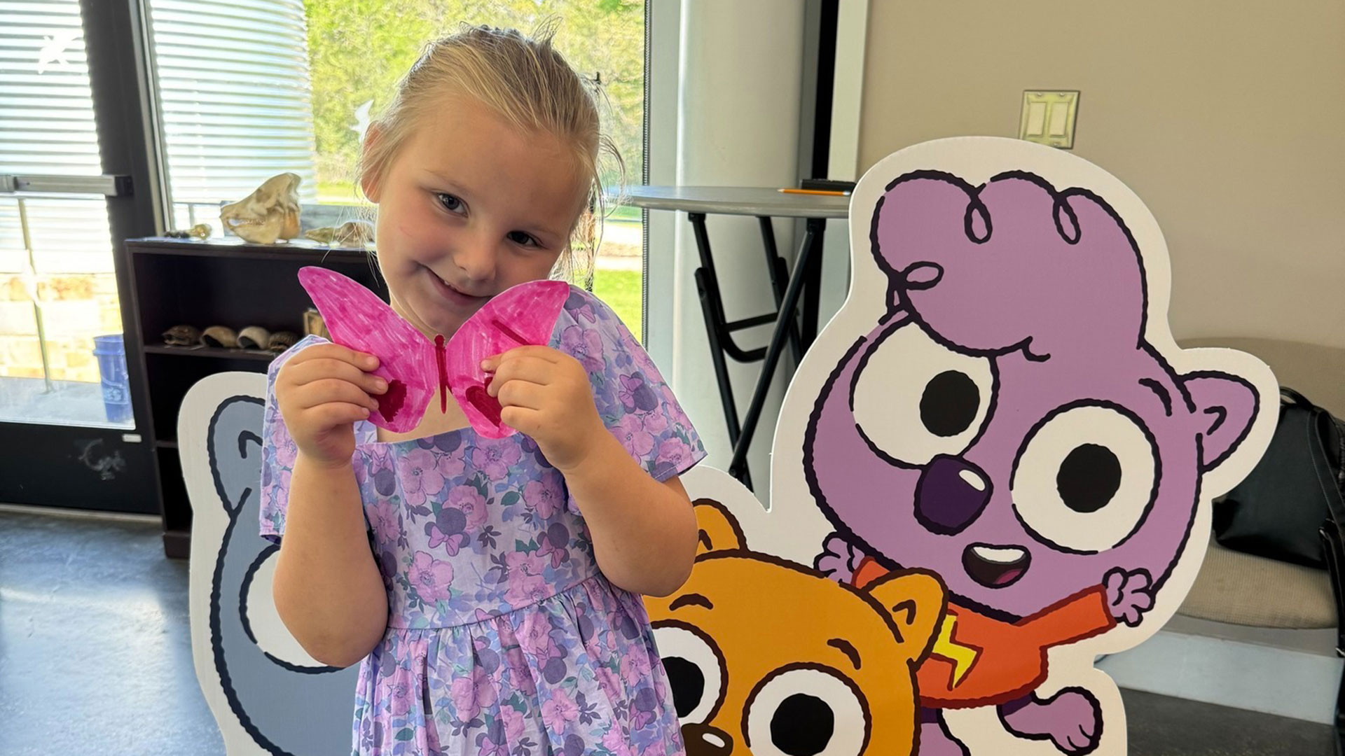 A child poses with her hand-made butterfly in front of a Work it out Wombats! standee