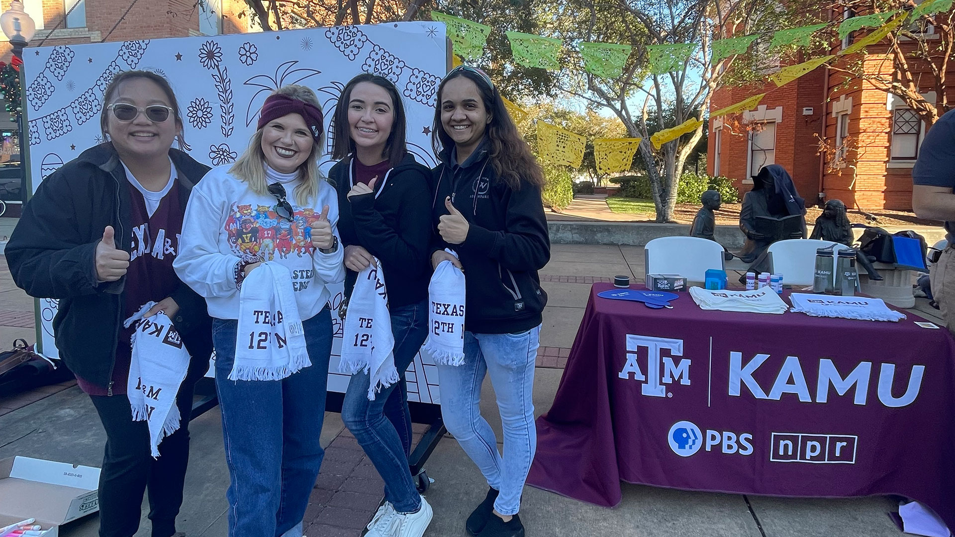 Four students flash a thumbs up with their KAMU-branded 12th Man towels