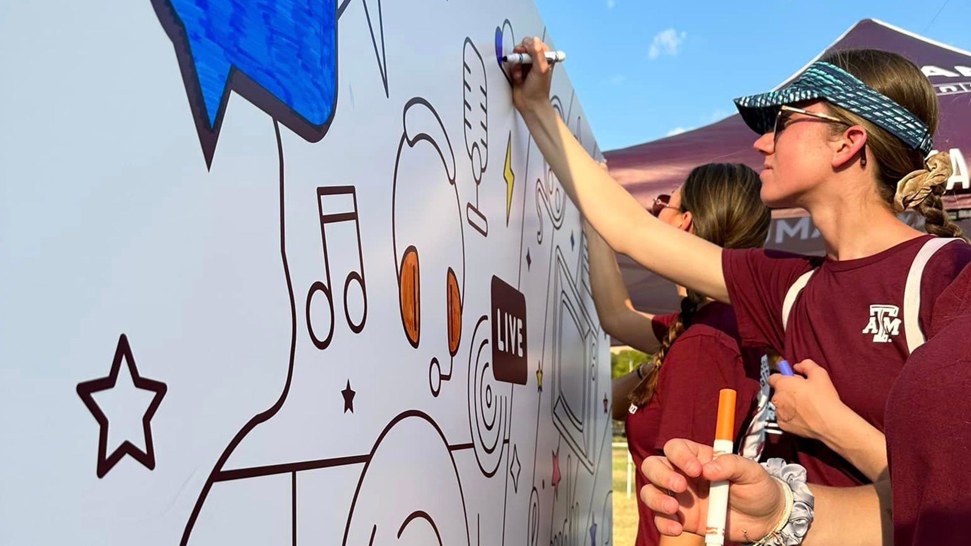 A student colors on the KAMU mural with a blue marker