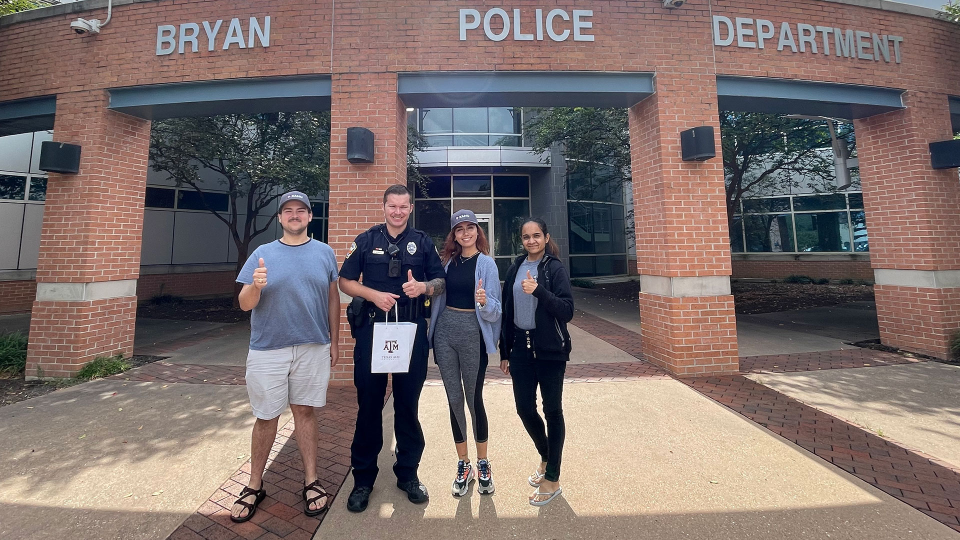 KAMU staff poses beside a cop outside of the Bryan Police Department