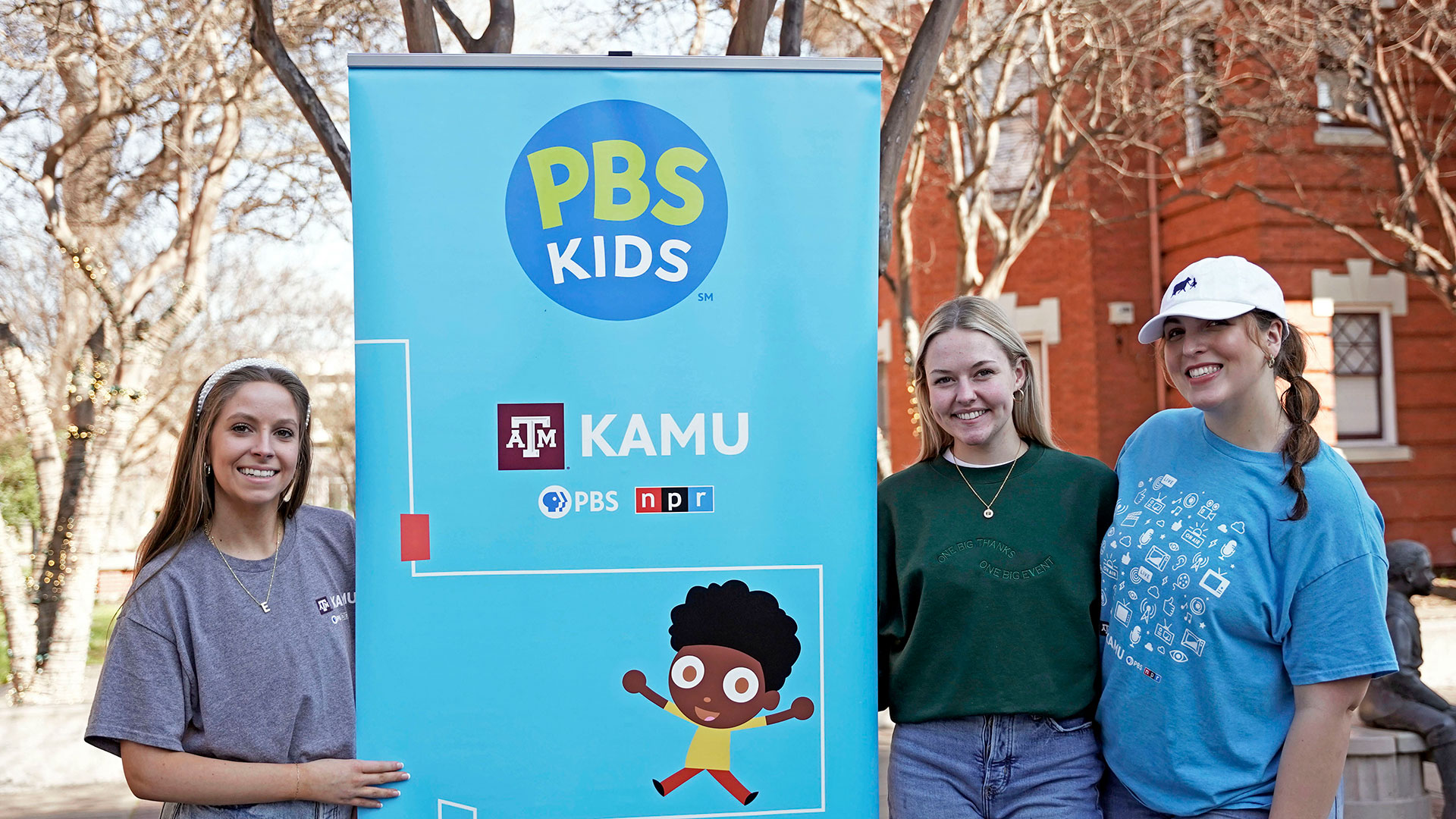 KAMU staff poses beside a PBS Kids and KAMU banner