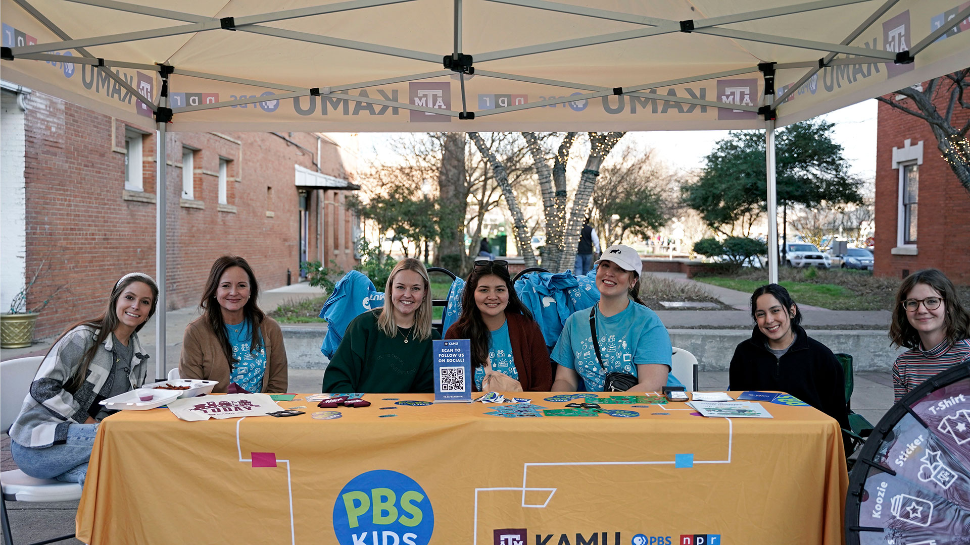 KAMU staff poses at a table with merchandise