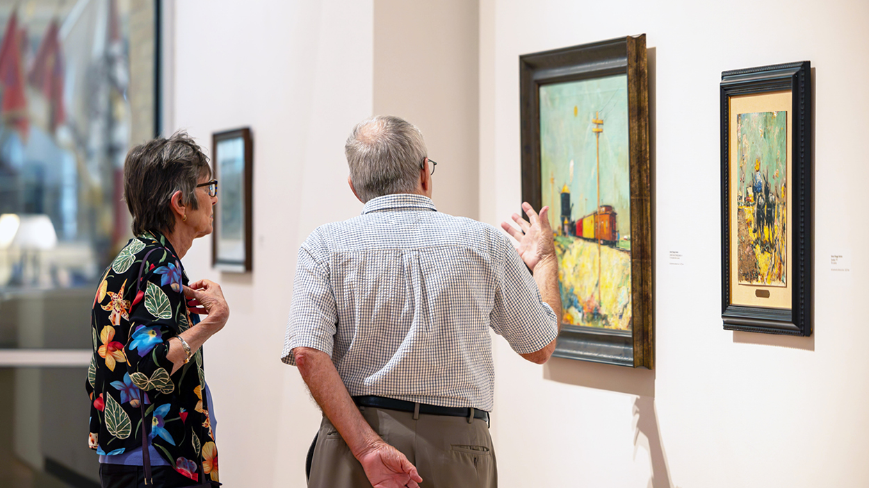 Two people look at a painting at the University Art Galleries.